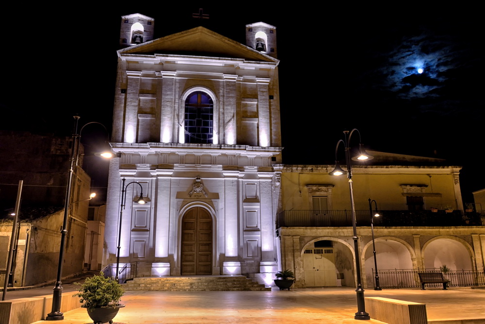 Chiesa illuminata di sera e palazzo con portico